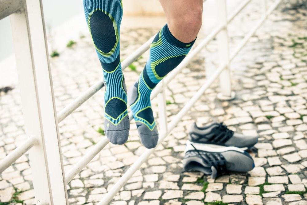 Mann mit blau-grauen Laufsocken sitzt auf einem Zaun und hat die Schuhe ausgezogen