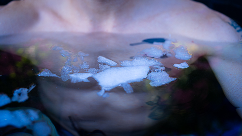berkörper beim Eisbaden mit Eisschollen auf der Wasseroberfläche Nahaufnahme des Oberkörpers einer Person beim Eisbaden, Eisschollen schwimmen auf der Wasseroberfläche vor der Brust.