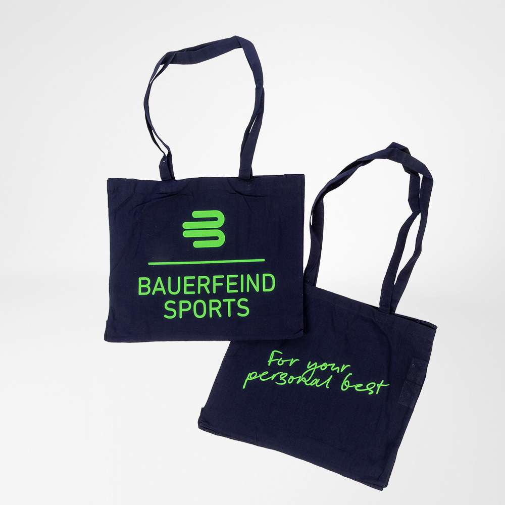 Zwei dunkelblaue Baumwolltaschen von Bauerfeind Sports mit neongrüner Aufschrift. Eine Tasche zeigt das Bauerfeind-Sports-Logo, die andere den Slogan „For your personal best“.