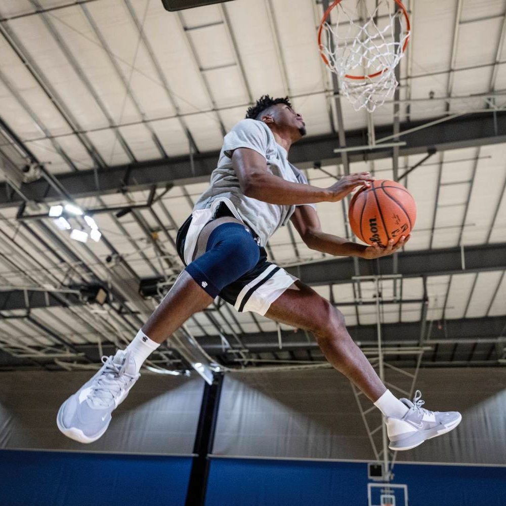 Ein Basketballspieler in der Luft beim Dunking, mit einer blauen Kniebandage am rechten Bein.