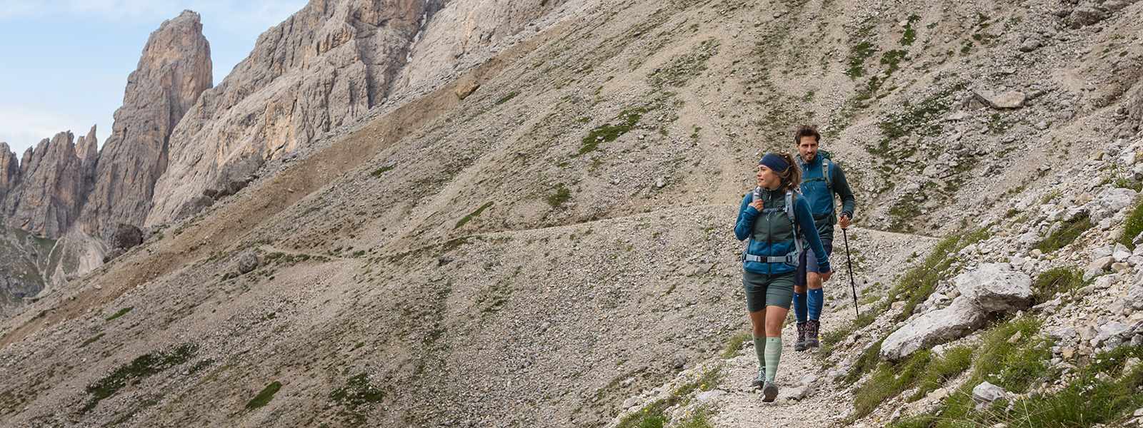 Mann und Frau wandern mit Wanderstöcken in der Hand einen Berg hinab und tragen dabei Wandersocken