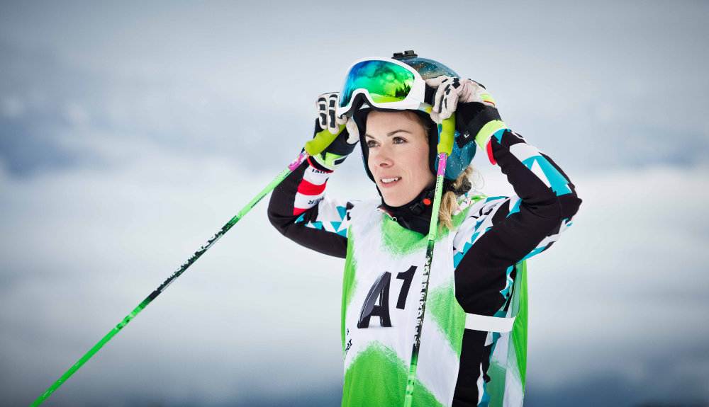 Skirennfahrerin Andrea Limbacher im blau-weiß-schwarzen Rennanzug richtet ihre Skibrille mit den Stöcken in den Händen