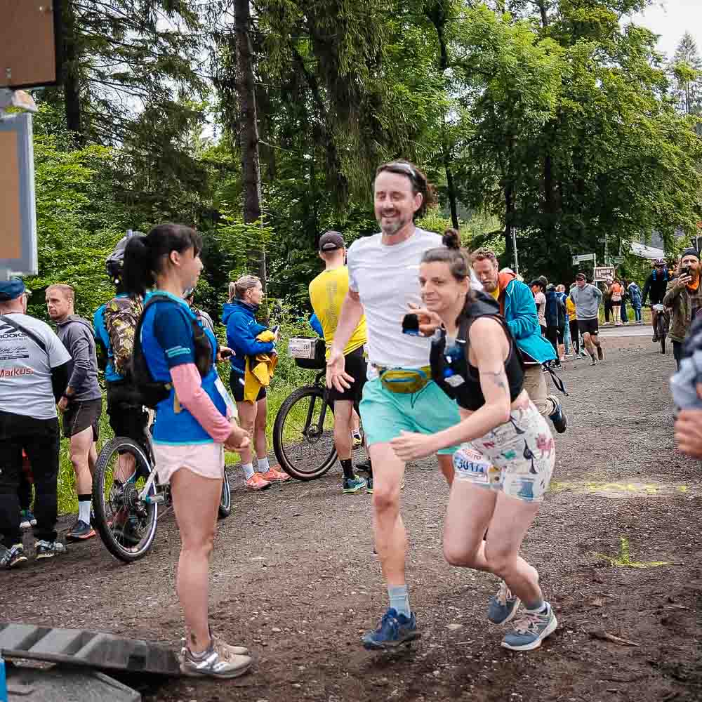 Gemeinsam zum Ziel laufen Ein Mann und eine Frau laufen gemeinsam, während im Hintergrund mehrere Menschen mit Fahrrädern stehen
