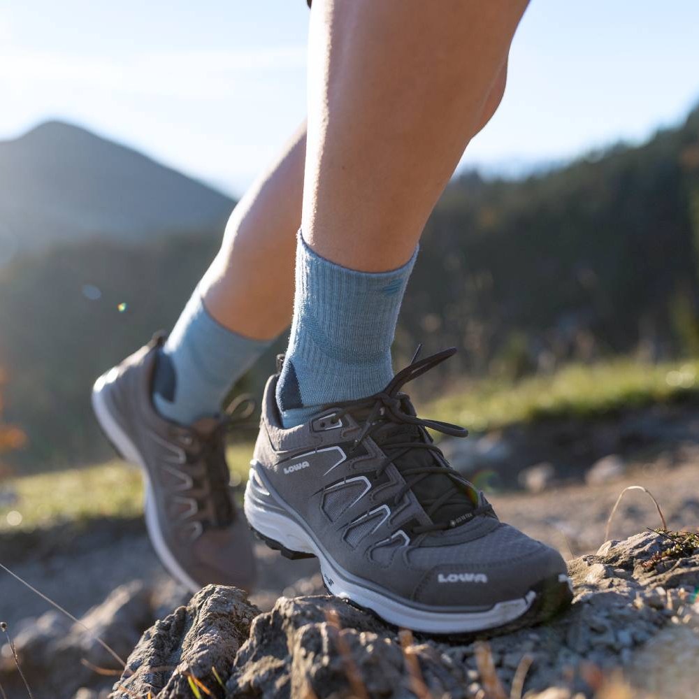 Hoch hinaus mit maximalem Komfort! Nahaufnahme eines Wanderers, der Merino Outdoor Socks in Granatfarbe trägt und einen felsigen Pfad hinaufsteigt. Die Socken sind in Wanderschuhen getragen und reichen bis zur Wade.