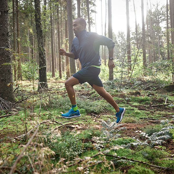 Ein Mann läuft durch einen dichten Wald und trägt dabei eine Achilles Bandage