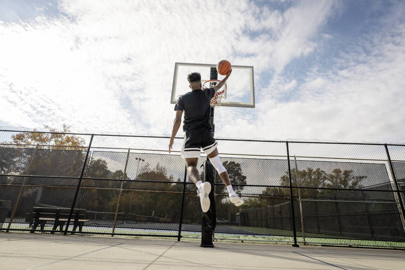 Basketballer mit weißer Kniebandage beim Dunking auf einem Streetballfeld