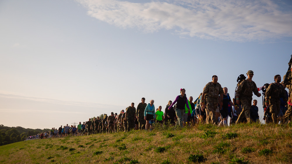 Wanderer und Soldaten in Uniform marschieren beim 4Daagse in einer langen Reihe über einen Deich im Morgenlicht.