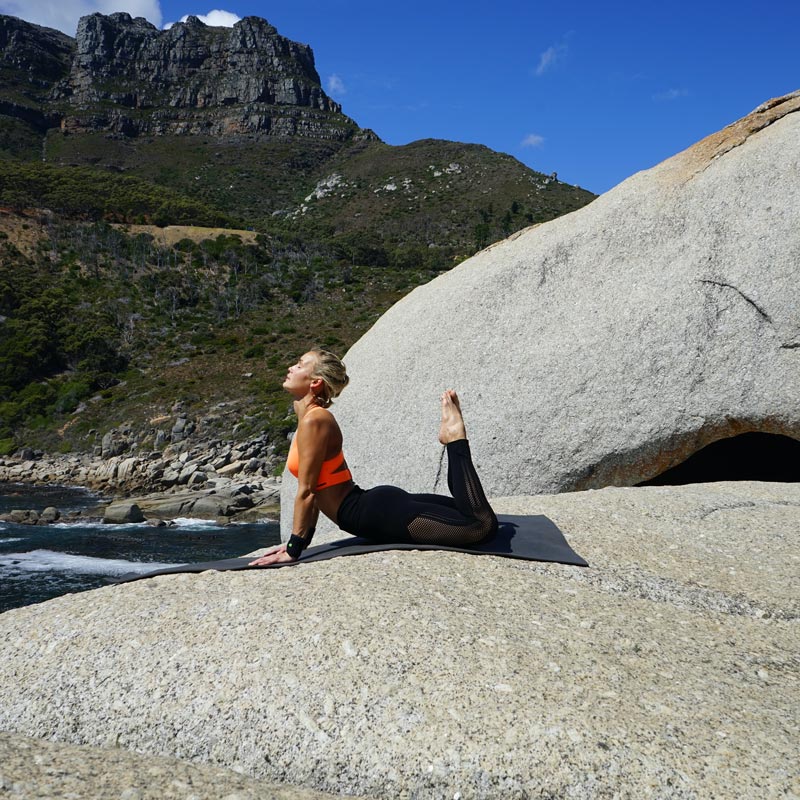 Frau beim Outdoor Yoga in der Königskobra-Pose hat die Hände aufgestützt und ihre Füße senkrecht nach oben gestreckt