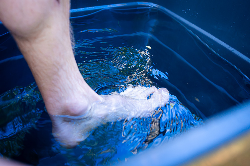 Erster Kontakt: Der Fuß wagt sich ins eisige Nass! Ein Fuß taucht in kaltes Wasser eines blauen Behälters ein. Das klare Wasser zeigt leichte Bewegungen und Lichtreflexionen an der Oberfläche.