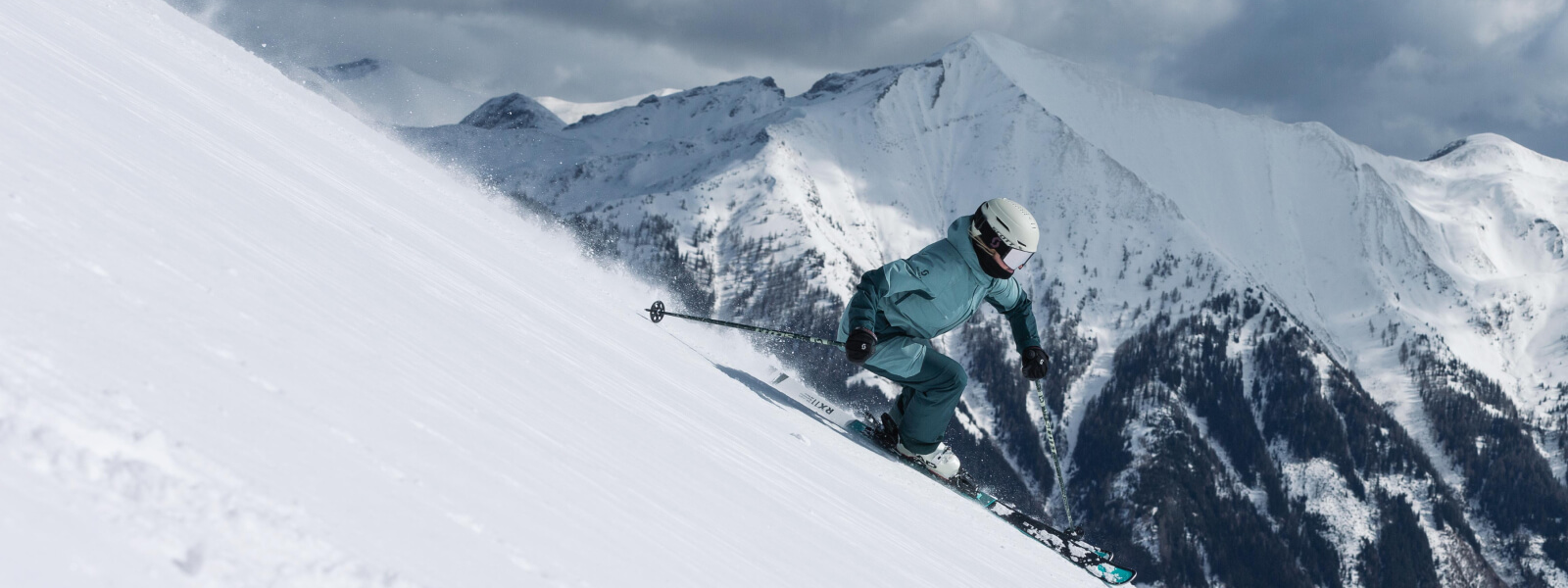 Skifahrer fährt eine Poste herunter, im Hintergrund befinden sich Schneebedeckte Berge