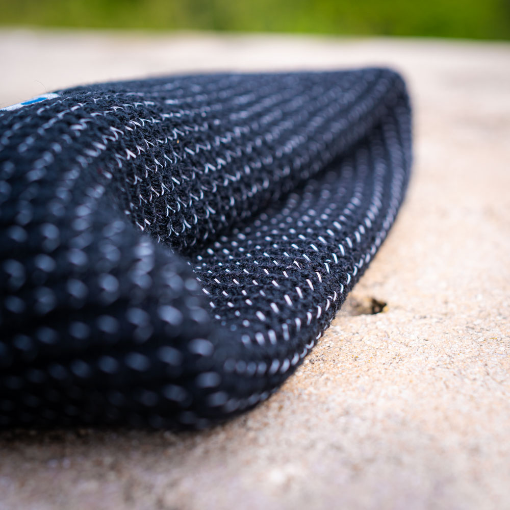 Robust und warm: Die Bauerfeind Sports Mütze für Outdoor-Abenteuer Eine gefaltete, schwarze Bauerfeind Sports Mütze liegt auf einem Stein, die grobe Struktur ist deutlich sichtbar.