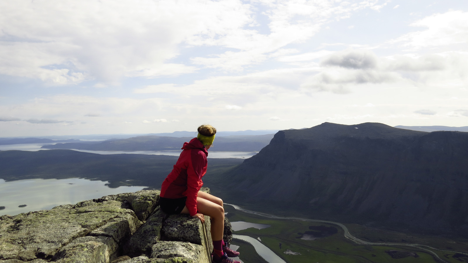Der knapp 1.200 Meter hohe Skierffe bietet fantastische Aussichten über Lappland Frau sitzt auf einem Felsvorsprung und schaut in die Ferne in Richtung Berge und Seen