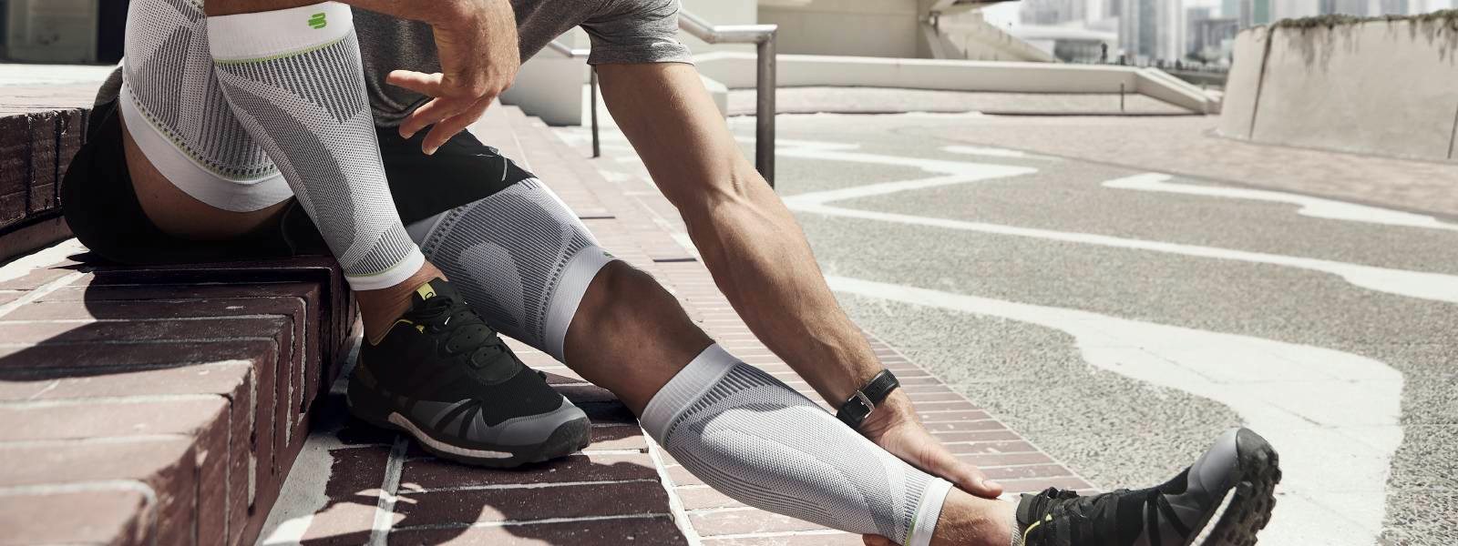 Sports Compression Sleeves Upper und Lower Leg weiß Mann ruht sich auf Stufen im urbanen Umfeld aus und trägt weiße Ober- und Unterschenkel-Sleeves