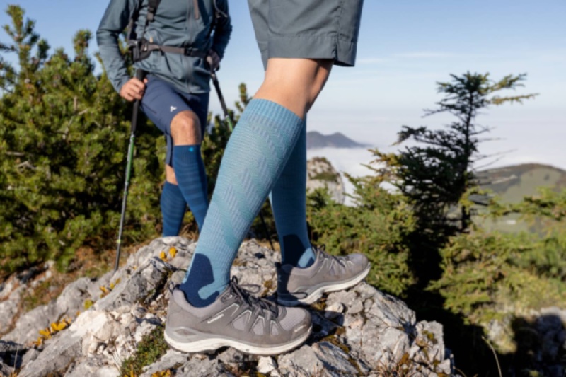 Zwei Wanderer mit Outdoor Merino Compression Socks auf einem felsigen Pfad. Diese Kompressionssocken bieten optimalen Komfort und Unterstützung für lange Wanderungen in natürlicher Umgebung.