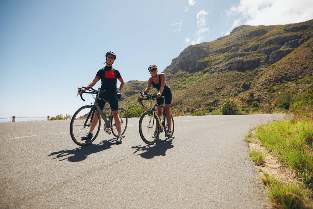 Ein Mann und eine Frau mit ihren Rennrädern stehen auf einer Straße im Gebirge