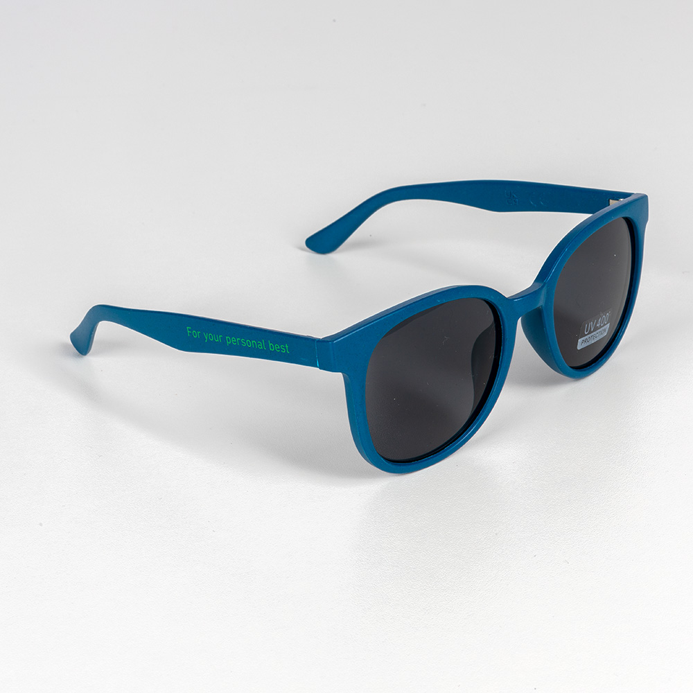 Blaugrüne Sonnenbrille mit dunklen Gläsern und dem grünen Aufdruck „For your personal best“ auf dem Bügel. Die Brille liegt auf weißem Hintergrund.
