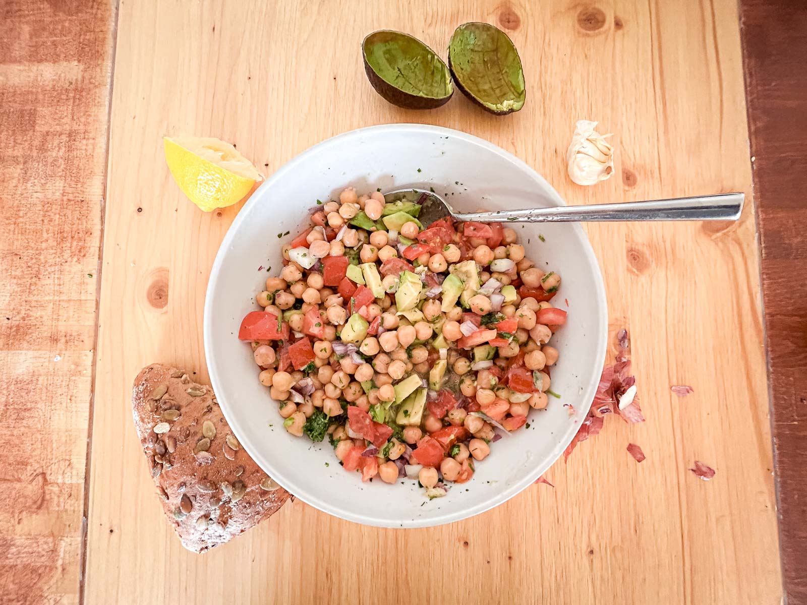 Kichererbsen-Salat – Gesunde und nahrhafte Mahlzeit nach dem Training. Eine Schale mit Kichererbsen-Salat, umgeben von frischen Zutaten wie Avocado, Zitrone und Brot. Ideal für eine gesunde und nahrhafte Mahlzeit nach dem Training.