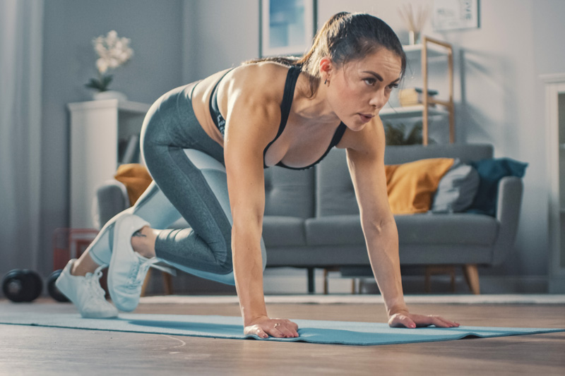 Krafttraining für Läufer: Ein paar Minuten zwischendurch reichen vollkommen aus Frau macht Mountain Climbers im Wohnzimmer	 im Hintergrund eine Couch und Regale