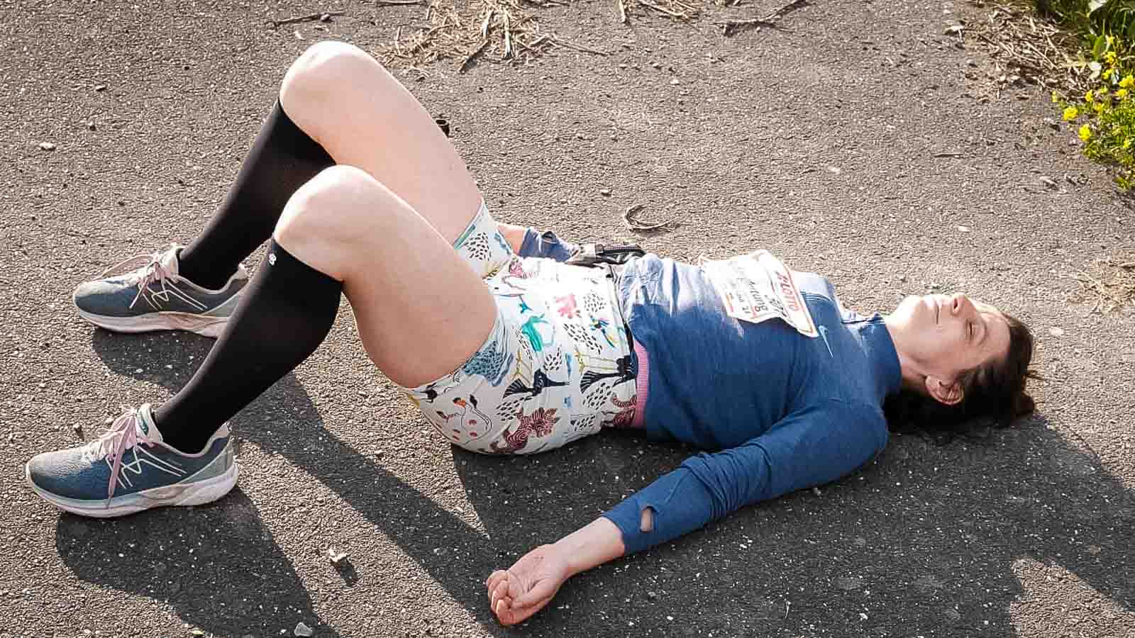 Nach dem Rennsteiglauf mit den Bauerfeind Recovery Socks entspannen Eine Frau mit knielangen Socken liegt nach dem Rennsteiglauf erschöpft auf dem Boden und hat ihre Beine angewinkelt