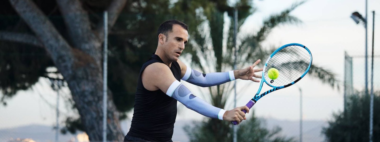 Tennisspieler mit weißen Arm Sleeves spielt Tennis und schlägt einen Ball mit der Rückhand