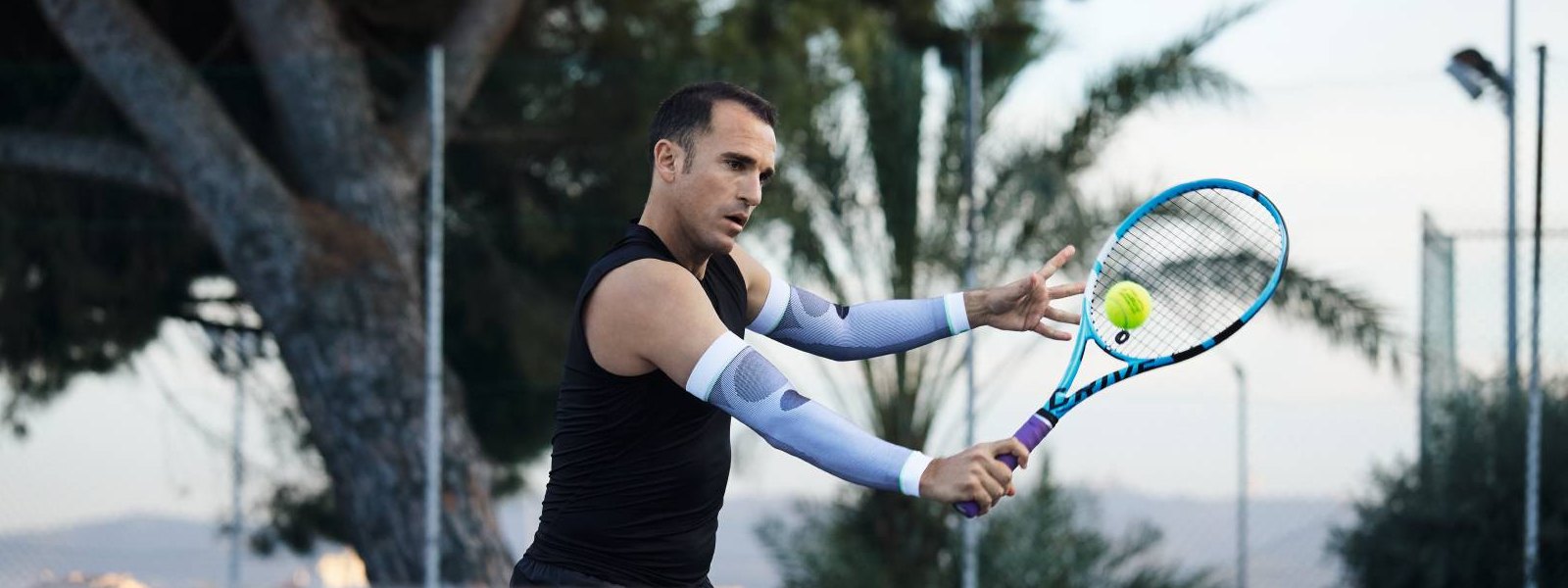 Arm Sleeves: dein perfekter Begleiter beim Tennis Tennisspieler mit weißen Arm Sleeves spielt Tennis und schlägt einen Ball mit der Rückhand