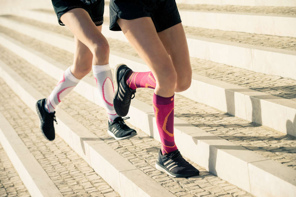 Zwei dünne Läuferbeine mit weißen und pinken Laufsocken laufen leicht schräg versetzt steinerne Stufen nach oben