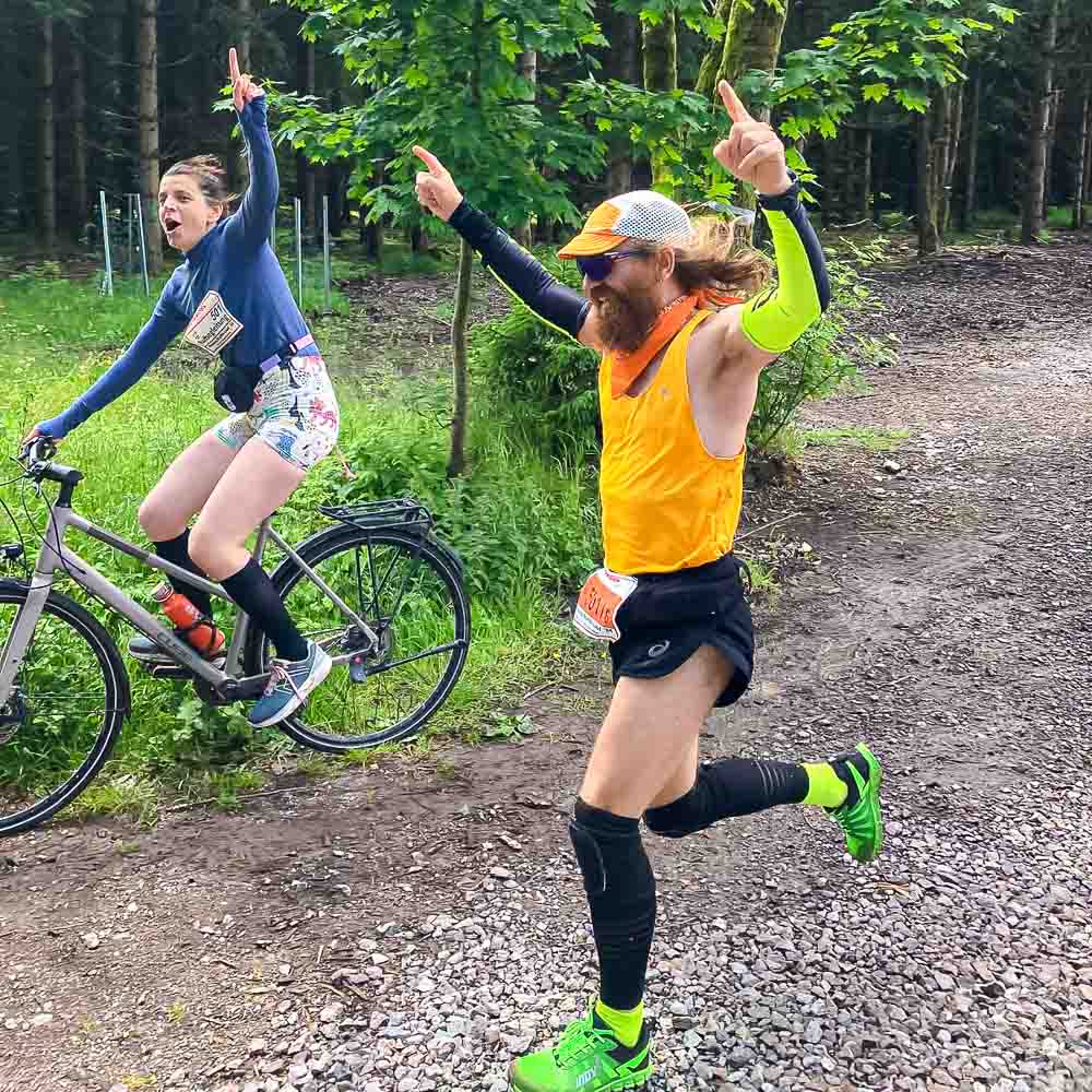 Mit dem Fahrrad und per Fuß jubelnd ins Ziel Ein Mann rennt jubelnd ins Ziel während eine Frau jubelnd auf dem Fahrrad nebenher fährt