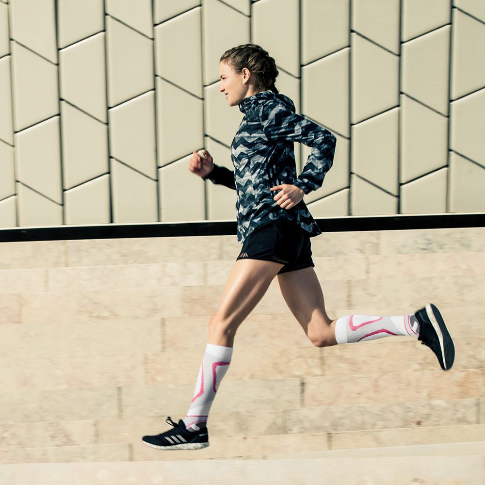 Läuferin mit weiß-rosa Laufsocken läuft neben einer modernen Mauer