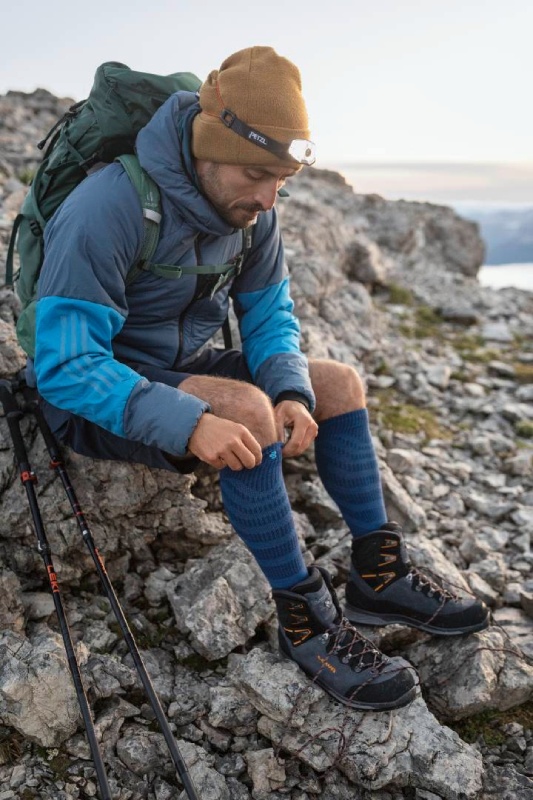 Lächelnde Wanderin mit Cappy und langen Wandersocken sitzt inmitten eines Feldes gelber Blumen