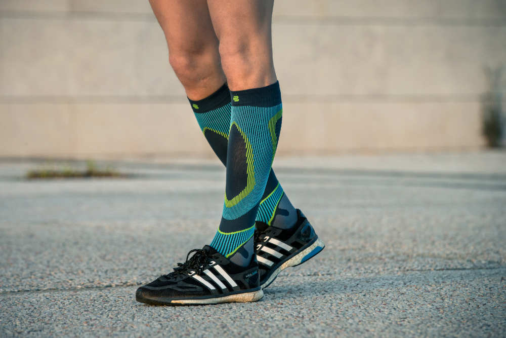 Unterschenkel eines Läufers in Nahaufnahme mit blau gemusterten Laufsocken auf einem Betonuntergrund