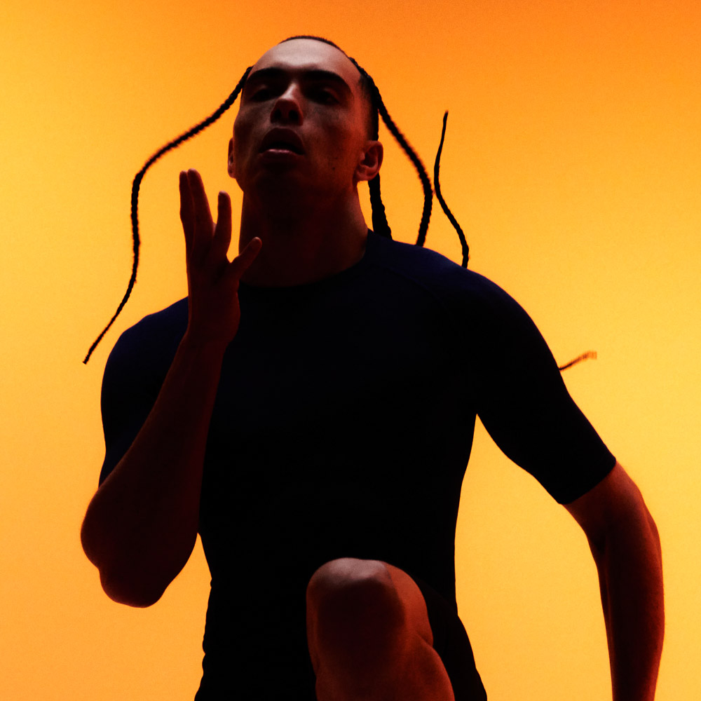 Ein Mann mit Braids macht Kniehebelauf vor orangefarbenen Hintergrund