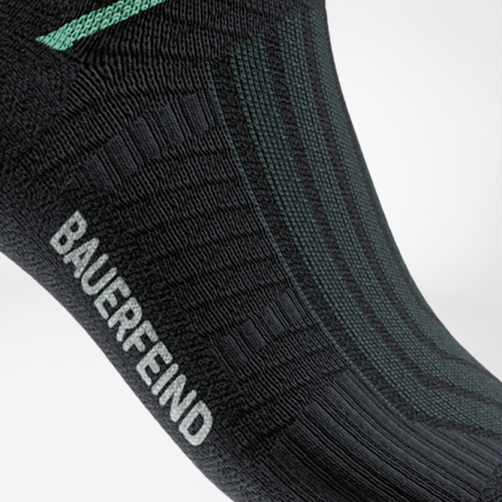 Detailansicht der Run Performance Midcut Socks in Schwarz mit grünem Arch-Lift-Element. Die Nahaufnahme zeigt die strukturierte Kompressionszone am Fußgewölbe, die für gezielten Halt und Unterstützung sorgt.