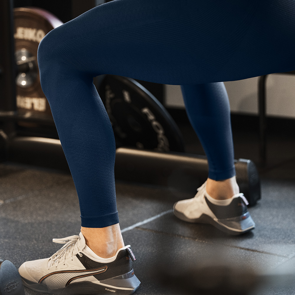 Stabilität von Grund auf – Kompressionstights für dein Beintraining Nahaufnahme der Beine eines Sportlers in blauen Kompressions-Tights während einer Übung im Fitnessstudio. Die Tight liegt eng an und fördert Stabilität und Durchblutung.