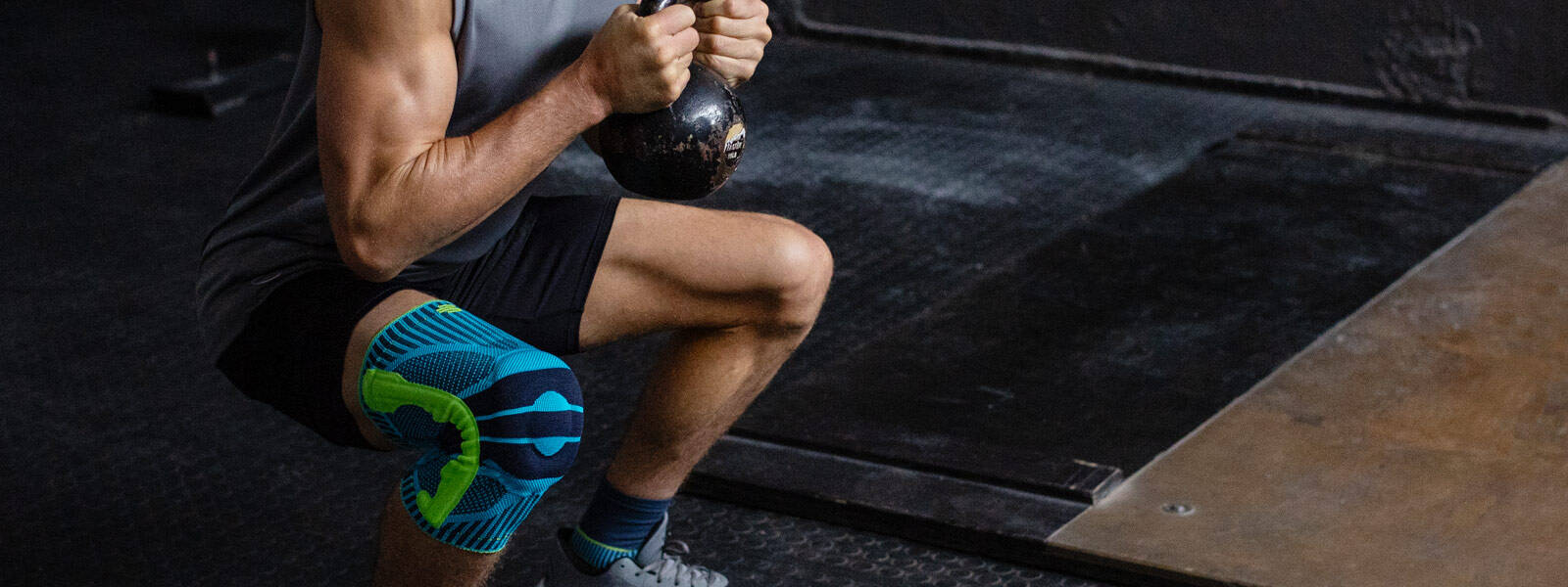 Mann mit Kniebandage geht in die tiefe Hocke mit einer Kettlebell zwischen beiden Händen