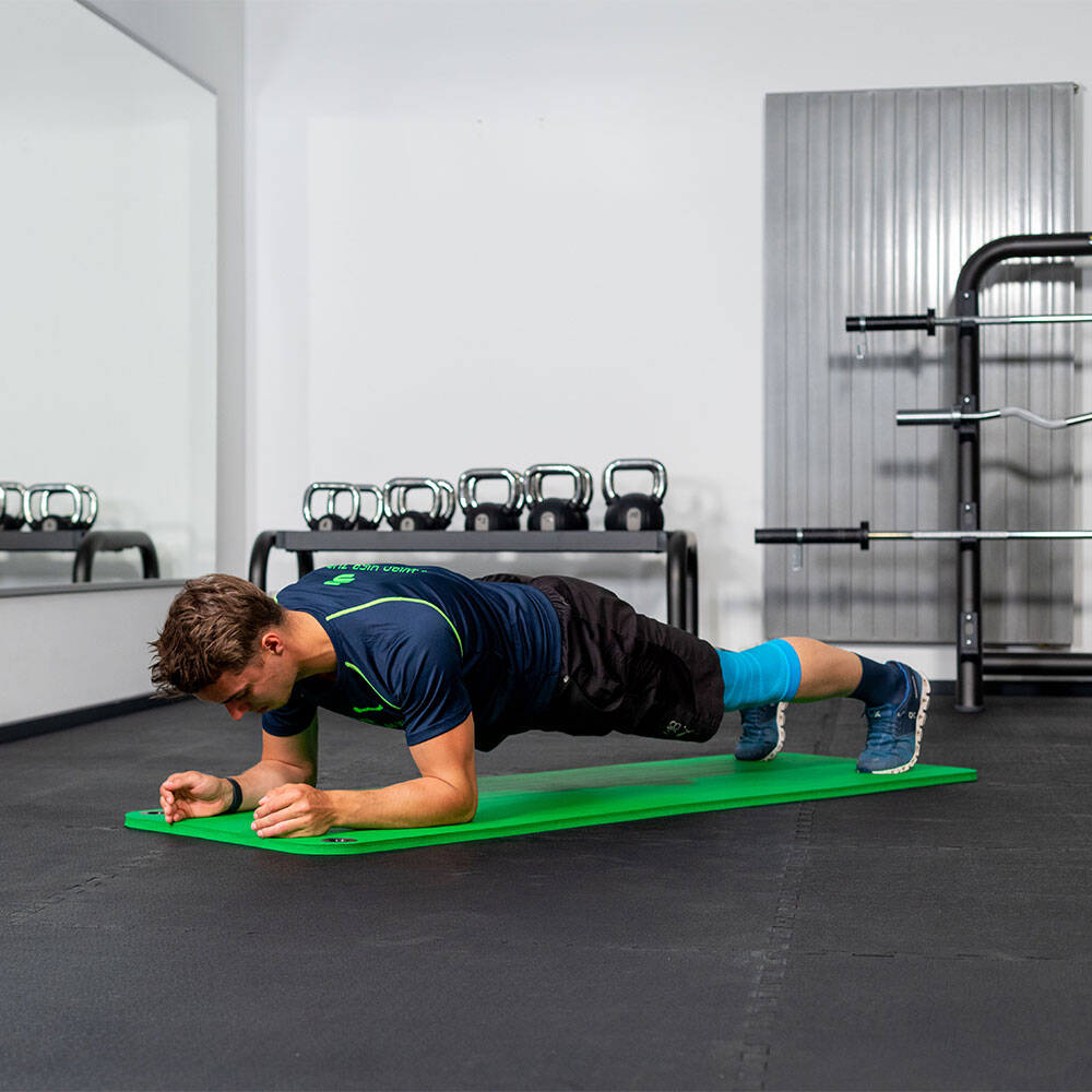 Mann im Fitnessstudio hält einen Unterarm Plank auf einer Fitnessmatte