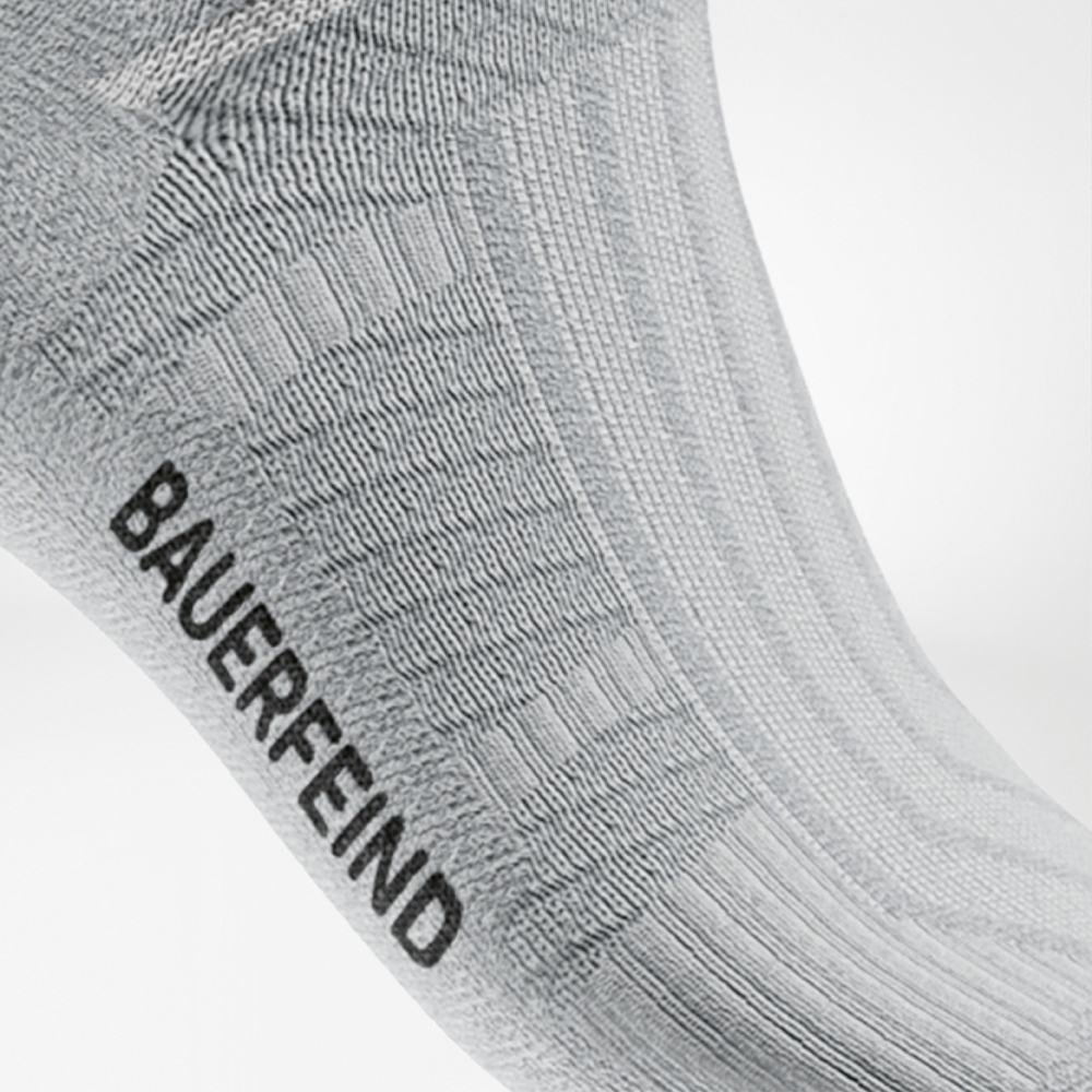 Seitlicher Blick auf eine weiße Sportsocke mit gut sichtbarer, integrierter Rippstruktur am Mittelfußbereich und schwarzem „BAUERFEIND“-Schriftzug – unterstützt das Fußgewölbe beim Laufen.