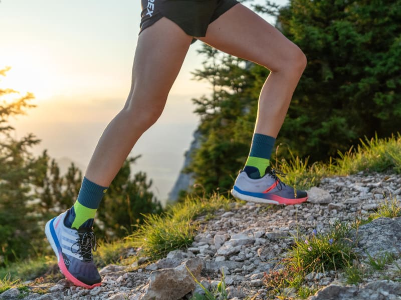 Läuferin mit mittellangen Trail Run Socks läuft einen Berg hoch