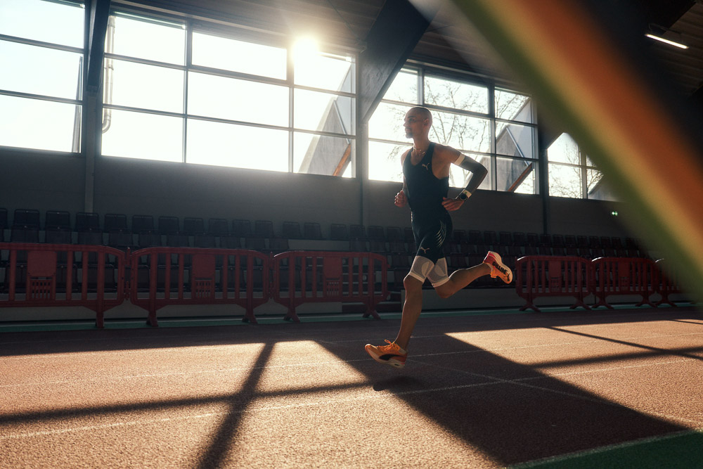 Marathonläufer Hendrik Pfeiffer trainiert auf einer Indoor-Laufbahn im Gegenlicht, mit Kompressions-Arm- und Beinsleeves für Stabilität und Leistung.