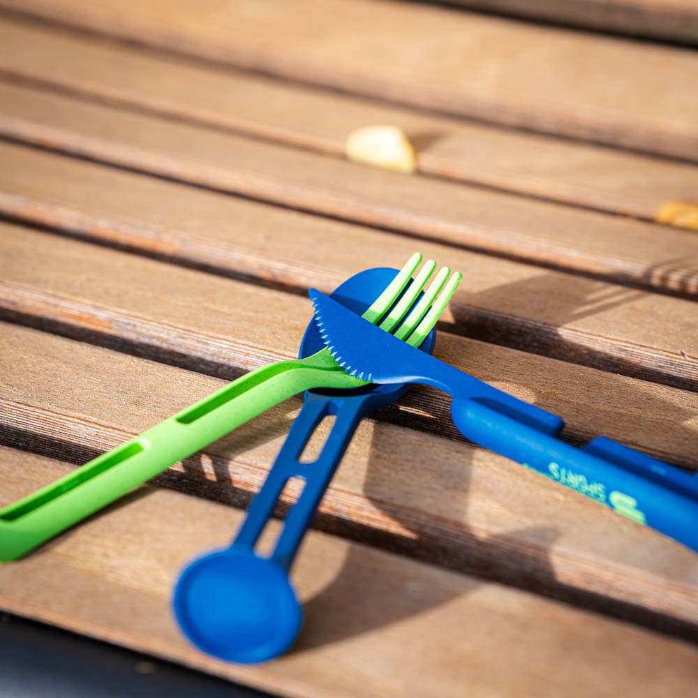 Cleveres Design: Outdoor-Besteck-Set für jedes Abenteuer Ein grünes und ein blaues Besteck liegen kreuzweise auf einer Holzbank. Das Set ist ideal für Outdoor-Essen und platzsparendes Packen.