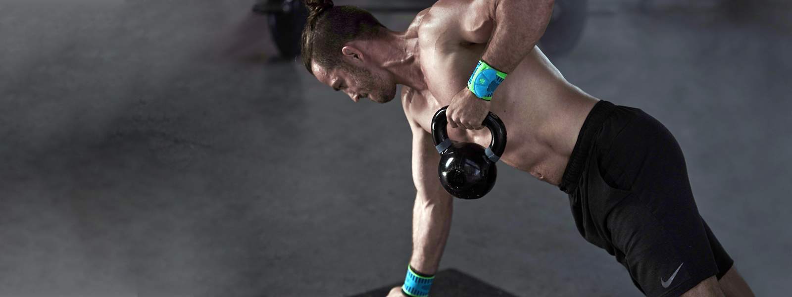 Kettlebelltraining - noch kraftvoller mit der Sports Wrist Strap Athletischer Mann mit freiem Oberkörper und Handgelenkbandagen trainiert mit der Kettlebell eine Hand stützt sich ab die andere zieht die Kettlebell nach oben