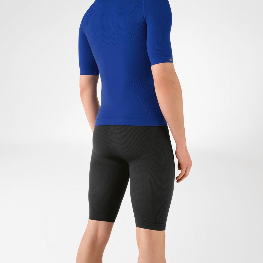 Der Mann trägt ein eng anliegendes, blaues Shirt, das seinen Oberkörper betont, sowie eine knielange, marineblaue, eng geschnittene Sporthose, die seinen Unterkörper umschließt.