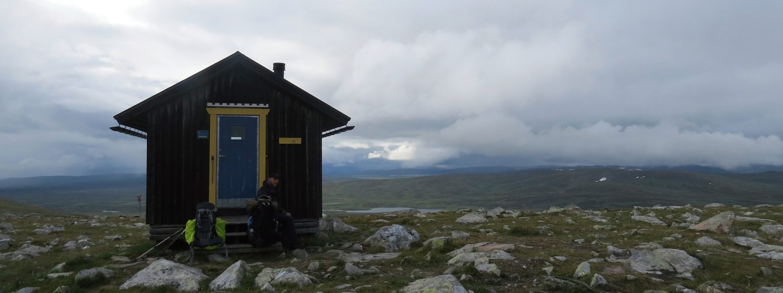 Markiere Dir kleine Landmarken wie diese Hütte, um ggf. auf einen Wetterumschwung reagieren zu können Eine einsame Hütte im Gebirge inmitten von begrasten Wiesen mit kleinen Felsen im Hintergrund die dichte Wolkendecke und ein kleiner Bergsee