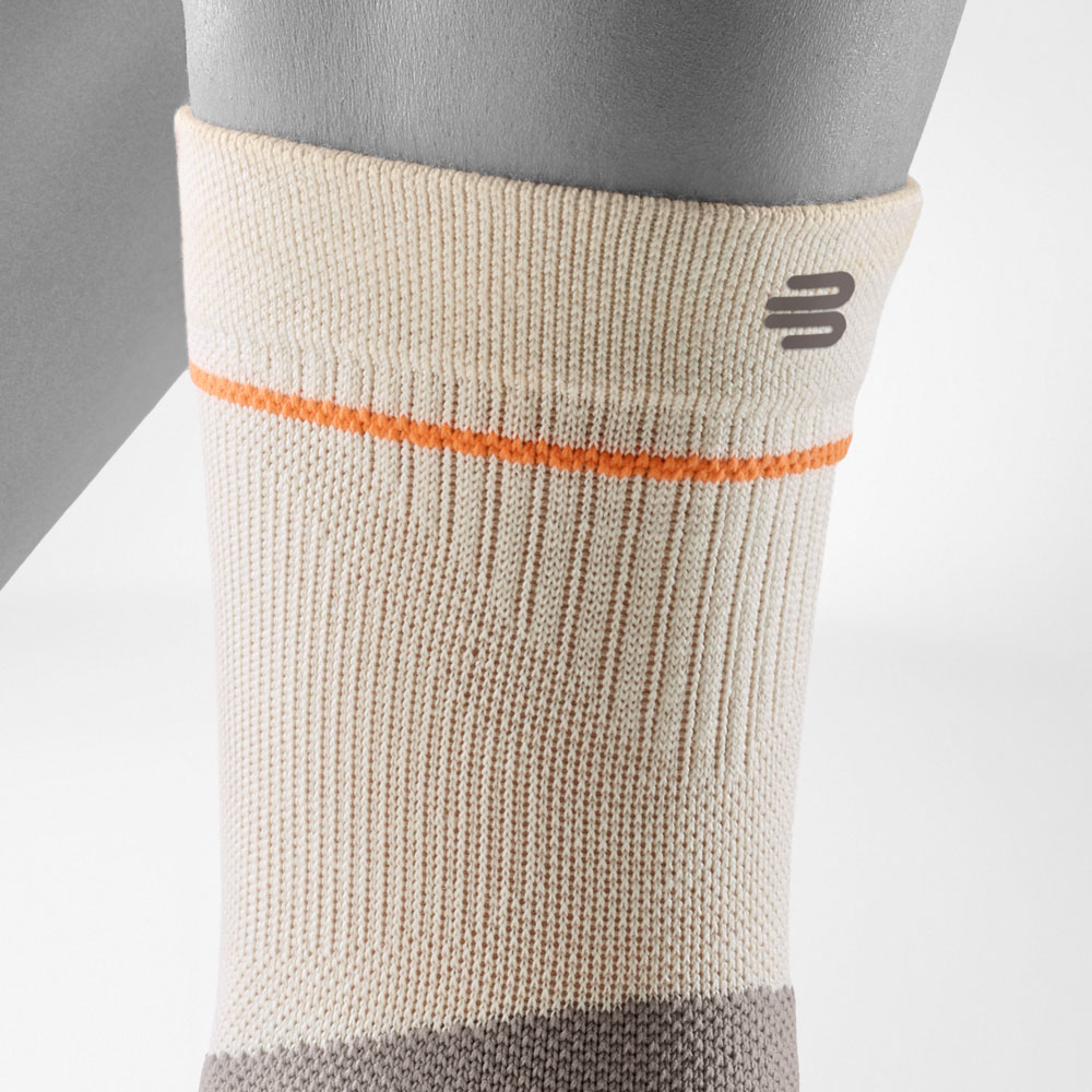 Detailaufnahme des oberen Schaftbereichs der Outdoor Compression Ankle Support in Sandstone. Sichtbar sind die enganliegende Passform, die feine Rippstruktur sowie das dezente Bauerfeind Sports Logo für sicheren Sitz beim Wandern.