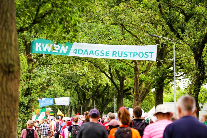 Rastpunkt beim 4Daagse Marsch Zahlreiche Teilnehmer passieren einen Rastpunkt beim 4Daagse Marsch. Über ihnen hängt ein großes Banner mit der Aufschrift „KWBN 4DAAGSE RUSTPOST“.