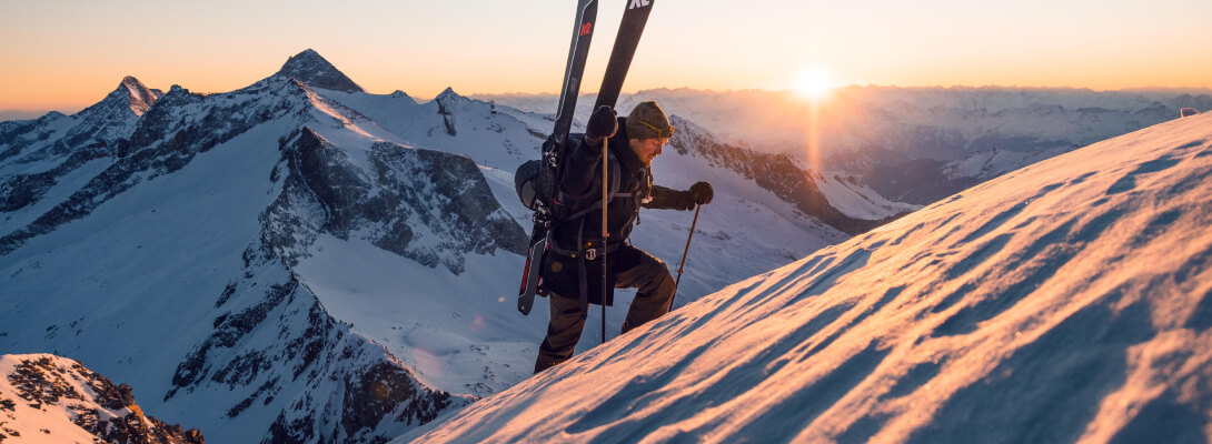 Skitouring Gänger erklimmt mit seinen Touringski auf dem Rücken den Berg