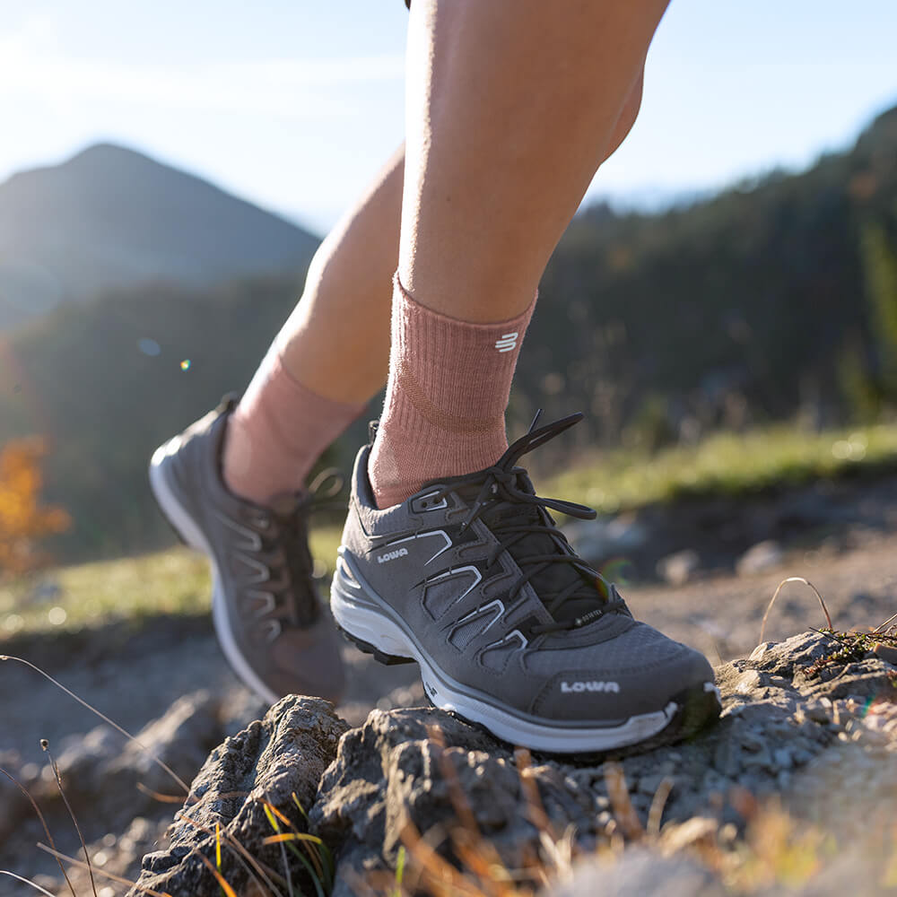 Nahaufnahme eines Wanderers, der Merino Outdoor Socks in Granatfarbe trägt und einen felsigen Pfad hinaufsteigt. Die Socken sind in Wanderschuhen getragen und reichen bis zur Wade.