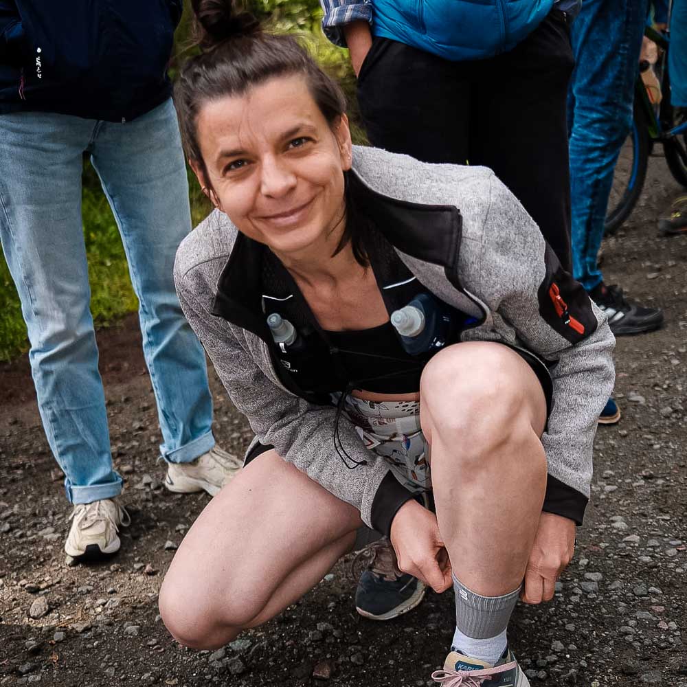 Vor dem Start des Rennsteiglaufes gut gelaunt die Trail Run Mid Cut Socks richten Eine Frau schaut lächelt in die Kamera und richtet dabei ihre mittellangen Trailrunsocken
