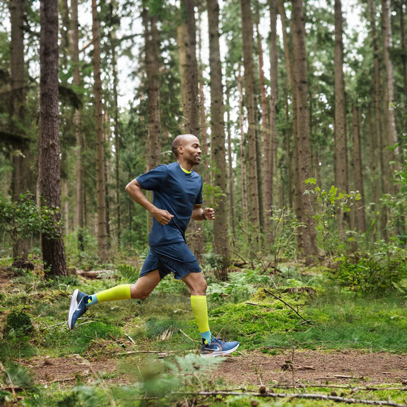 Ein Läufer rennt schnell durch einen dichten Wald und trägt dabei Kompressions-Socken