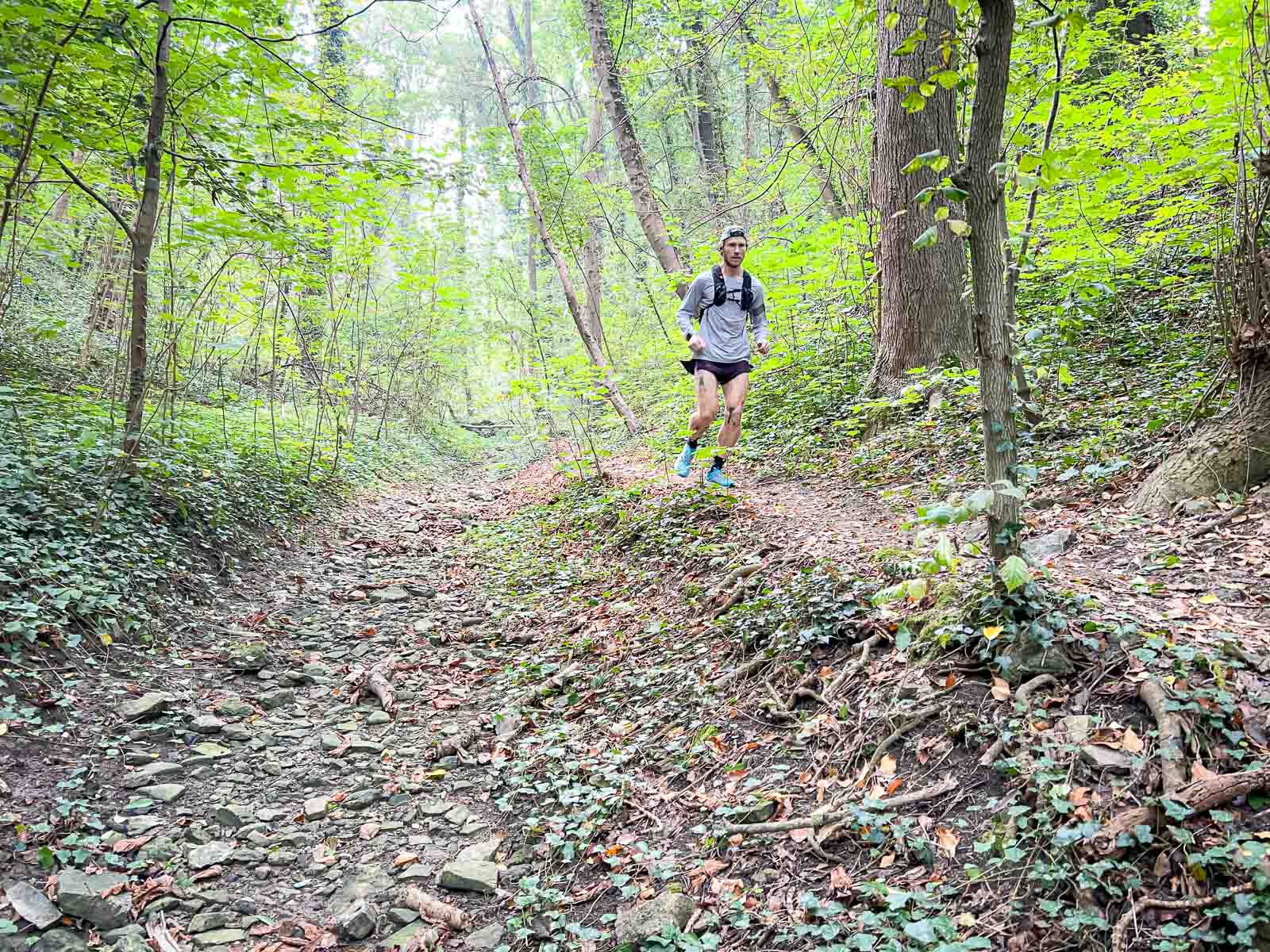 Trailrunning im Wald – Perfektes Training in der Natur. Ein Trailrunner läuft auf einem steinigen Pfad durch einen dichten Wald. Die Umgebung ist grün und ruhig, ideal für intensives Outdoor-Training.