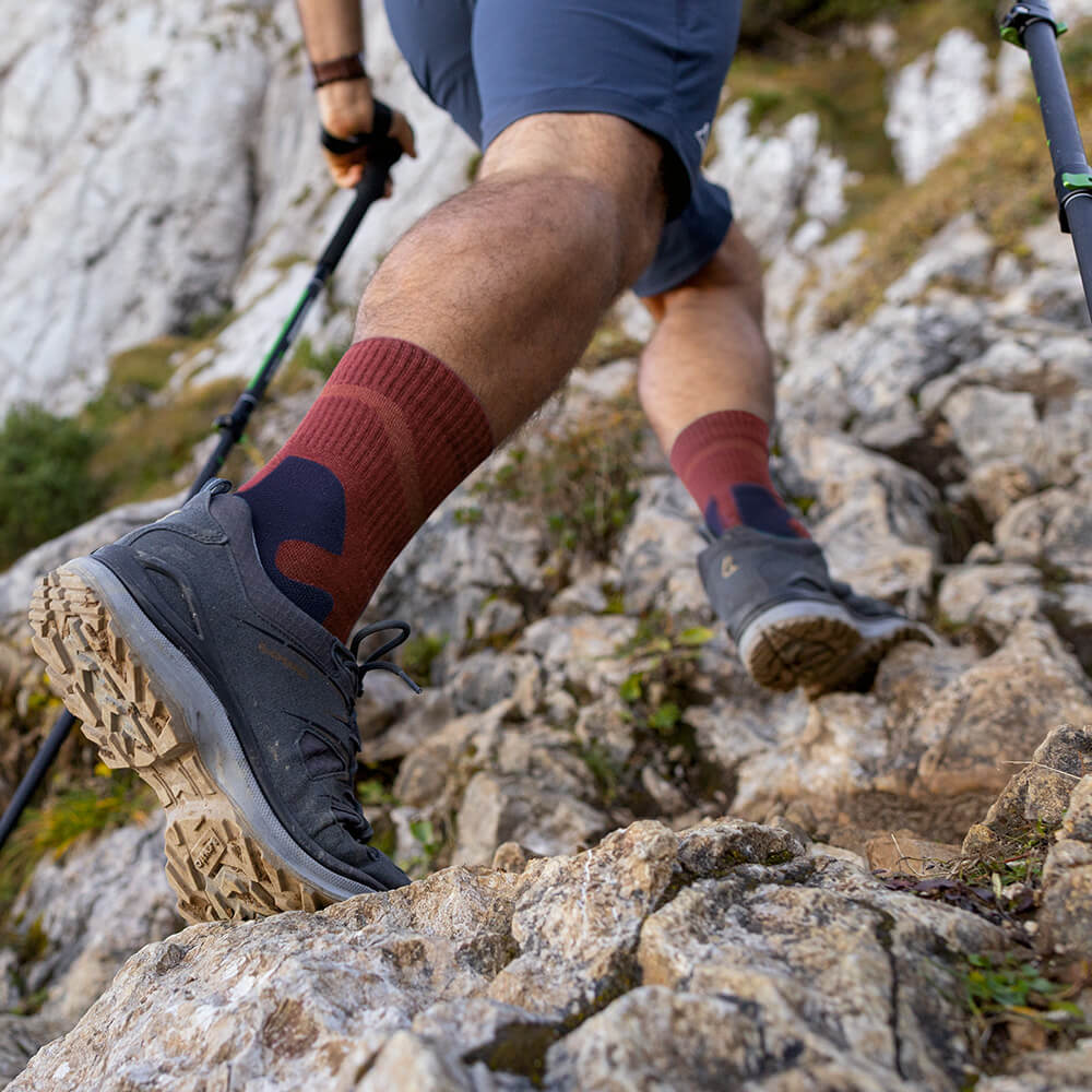 Nahaufnahme eines Wanderers, der Merino Outdoor Socks in Granatfarbe trägt und einen felsigen Pfad hinaufsteigt. Die Socken sind in Wanderschuhen getragen und reichen bis zur Wade.